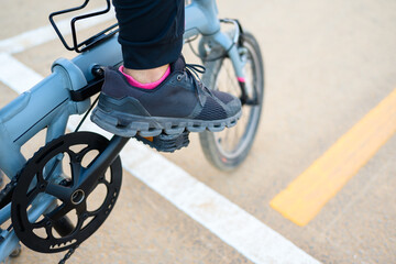 Obraz premium Closeup foot of a woman on the pedal of a folding bicycle, with traffic lines on the asphalt road
