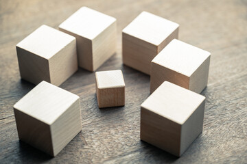 A small wooden cube under siege by many big wooden cubes, concept of a small business encircled by...