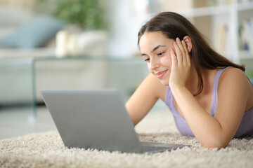 Satisfied woman on the floor watching videos on laptop - 755437818