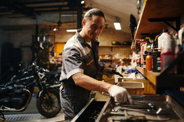 Smiling repairman taking tool from work bench in garage