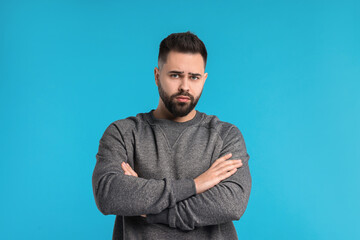 Portrait of sad man with crossed arms on light blue background