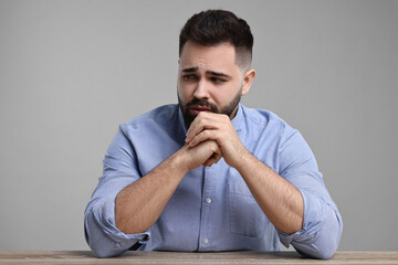 Portrait of sad man at wooden table on light grey background