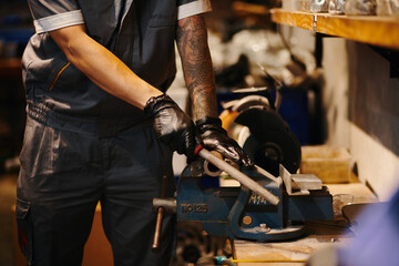 Mechanic sharpening edges of detail at repair shop workbench