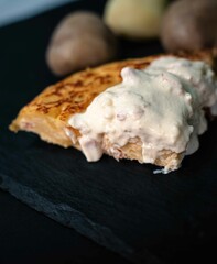 Spanish potato omelette with carbonara sauce, on a white plate, surrounded by the ingredients necessary to prepare it, potatoes, egg, onion and bacon
