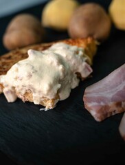 Spanish potato omelette with carbonara sauce, on a white plate, surrounded by the ingredients necessary to prepare it, potatoes, egg, onion and bacon