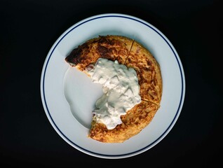 Spanish potato omelet made with olive oil, eggs, potatoes and carbonara sauce on a white plate on a black background. Spanish appetizer