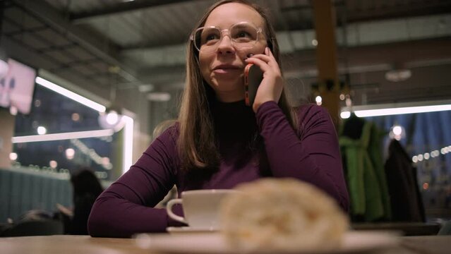 A woman is seated at a table, engaged in conversation on her cell phone in the cafe