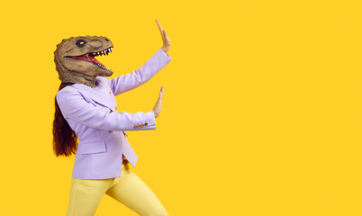 Elegant young woman in purple jacket and yellow pants with Tyrannosaurus Rex, dinosaur head mask,...