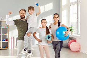 Portrait of happy cheerful sporty family with kids standing in gym with fit ball and yoga mat in...