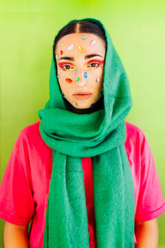 Woman with gem stickers on face wearing green scarf against green background