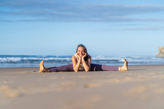Smiling woman practicing straddle yoga pose at beach