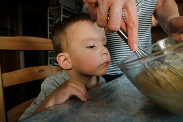 Curious grandson learning process of stirring dough with grandmother at home