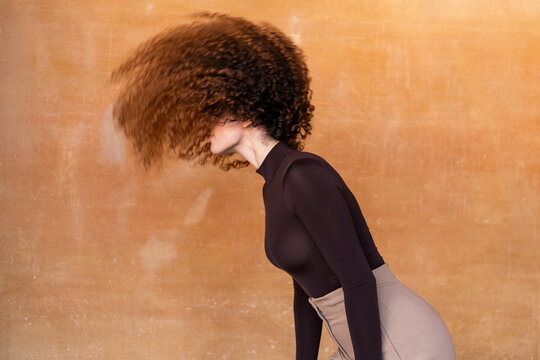 Young woman flipping hair against brown background