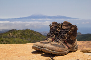 Spain, Canary Islands, La Gomera, Pair of brown hiking boots standing at summit of Garajonay with Teide volcano looming in distant background