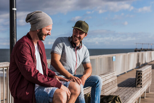 Happy young friends sitting and laughing on bench in city