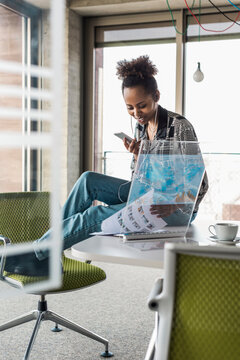 Young businesswoman with smart phone examining document in office
