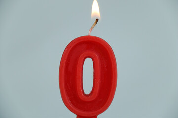close up on a red number zero birthday candle with fire on a white background.

