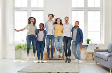 Group portrait of cheerful mixed race people friends jumping up and posing for photo and smiling looking at camera in modern living room at home. Friendship, hanging out, lifelong friends concept.