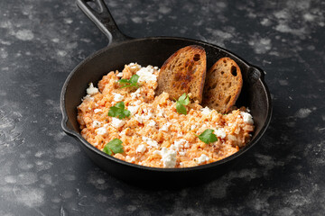 Strapatsada, eggs scrambled with bread, tomatoes and feta cheese in iron cast pan. Greek breakfast - obrazy, fototapety, plakaty