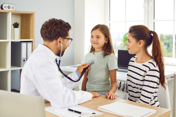 Children healthcare. Professional male pediatrician doctor checks heartbeat and breathing of little girl. Doctor with stethoscope examines child brought by his mother for examination.