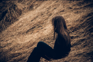 girl in black sits in dry grass