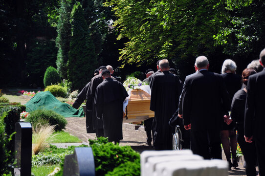 Beerdigung mit Trauerzug: Der Sarg wird von Tr&auml;gern zur Grabstelle auf dem Friedhofsplatz getragen. 