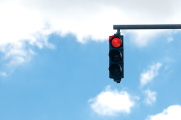 Red traffic light on blue cloudy sky background