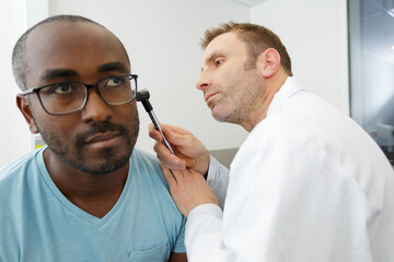 male doctor checking patients ear using otoscope