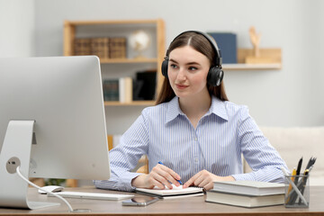 E-learning. Young woman taking notes during online lesson at table indoors