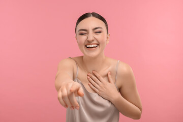 Beautiful woman pointing at something and laughing on pink background