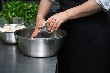 Close-up of female hands grating champignons into a bowl on the table.