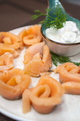 Close-up of pickled salmon pieces on a white plate with sauce and dill on the table. Beautiful serving of pickled salmon. Vertical photo.