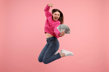 Happy woman with dollar banknotes jumping on pink background
