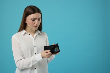 Sad woman showing empty wallet on light blue background, space for text