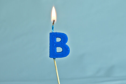 close up on a blue letter B birthday candle with fire on a white background.
