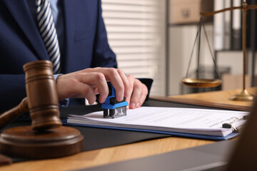 Notary stamping document at wooden table in office, closeup