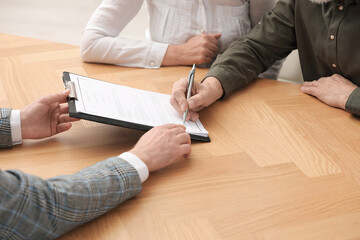 Notary showing senior couple where to sign Last Will and Testament at wooden table indoors, closeup