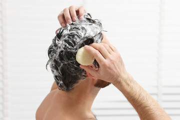 Man washing his hair with solid shampoo bar in shower, closeup