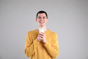 Happy man with milk mustache holding glass of tasty dairy drink on gray background