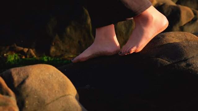 a slow-motion video depicting a teenage girls feet with painted toenails, her dog, balancing on rocks by the tidepool on a pacific coast beach in california