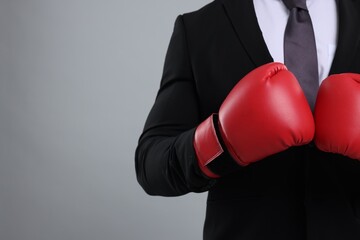 Businessman in suit wearing boxing gloves on grey background, closeup. Space for text