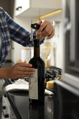 Woman opening wine bottle with corkscrew at black countertop indoors, closeup