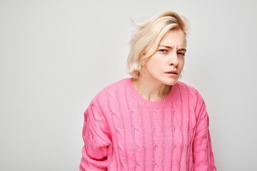 Woman in pink sweater looking away with a thoughtful expression, isolated on a light background.