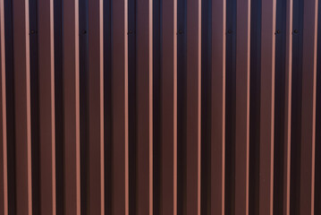 Background of brown metal profile fence. Building material metal tile or corrugated profiled sheet. Close-up.