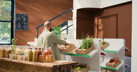 Client choosing bio produce to buy, approaching checkout counter to pay for bag filled with organic freshly harvested vegetables. Person going shopping for groceries at local natural market.