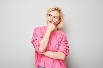 Thoughtful young person on gray background, with a contemplative expression and hand on chin.