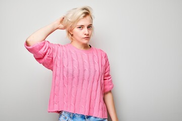 Portrait of a young woman in a pink sweater posing casually with a hand in hair on gray background.