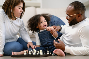 Adorable afro hair kid playing chessboard toy with her parent. Multiracial family enjoying game...