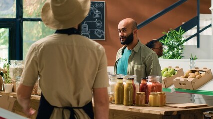 Shop owner presents pasta types to client, opening sustainable containers filled with bulk products in natural eco grocery store. Vendor recommending organic chemicals free food items.