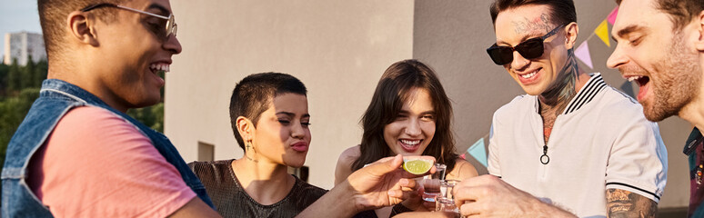 jolly multicultural friends drinking tequila with fresh lime and salt at rooftop party, banner